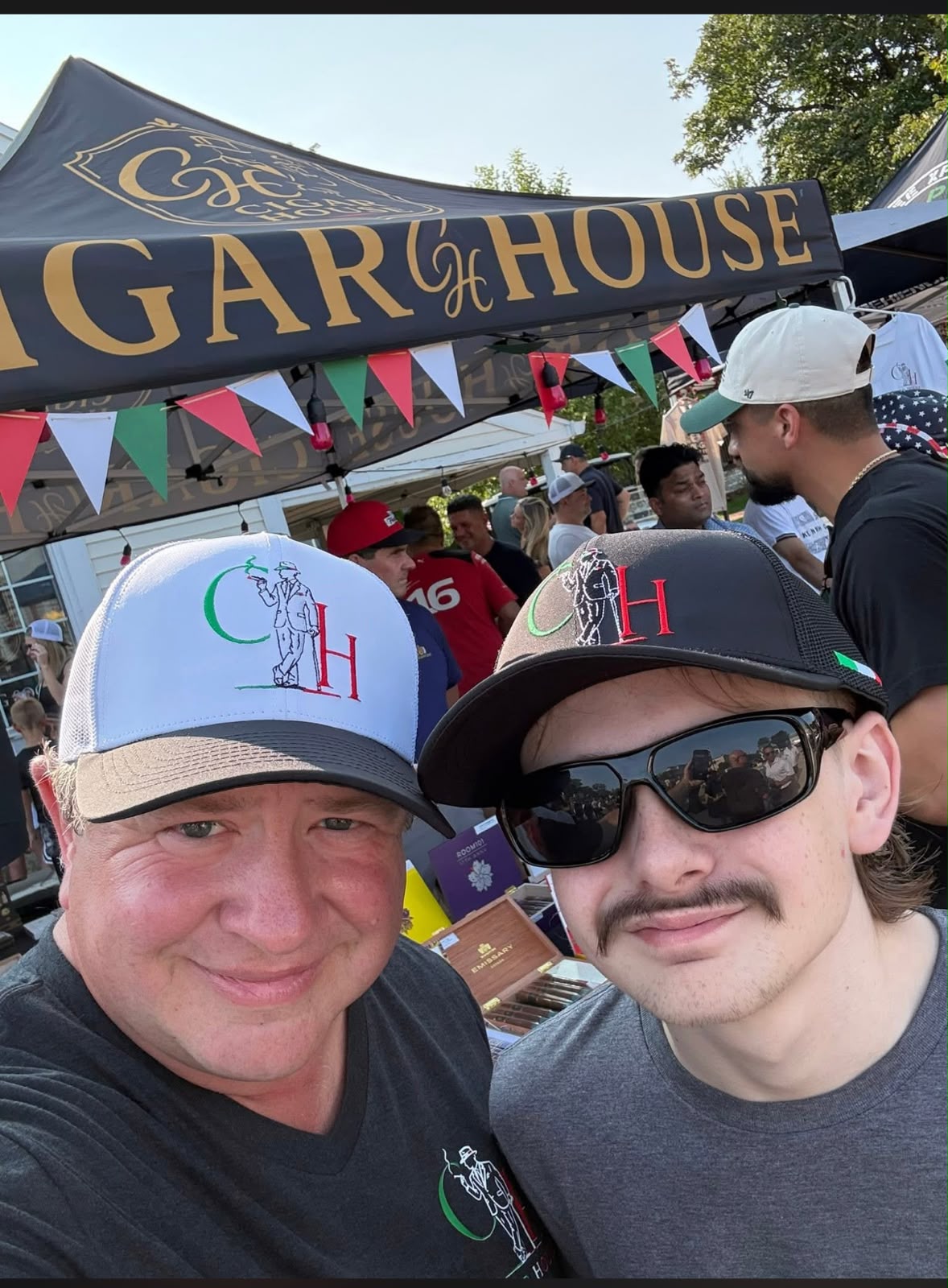 The gold-lettered Cigar House tent banner above the cigar stand at the Old Town Italian Fest in Bloomingdale, with team members in CH caps
